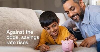 Father and son gathered around piggy bank next to words "Against the odds, savings rate rises"